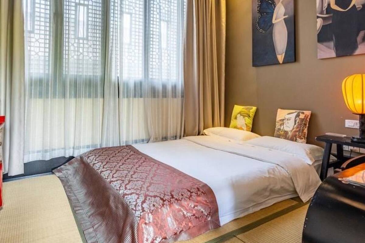 Une chambre d’hôtel avec un lit, des rideaux, une lampe et des œuvres d’art accrochées au mur.
