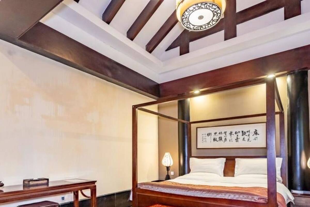 Une chambre à coucher de style traditionnel, avec un lit à baldaquin, un bureau et un banc décoratif rouge.