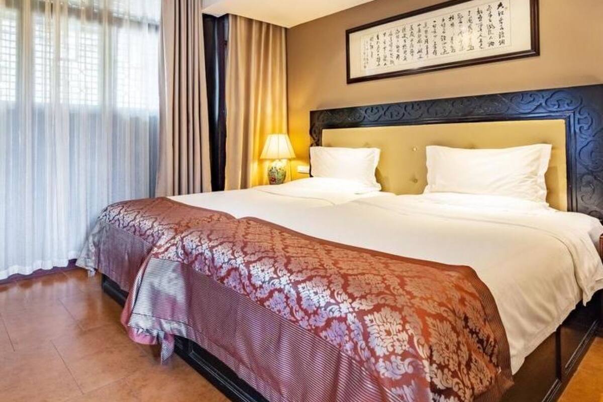 Une chambre d’hôtel avec un grand lit, une table de chevet avec une lampe, une œuvre d’art encadrée au mur et une fenêtre avec des rideaux.