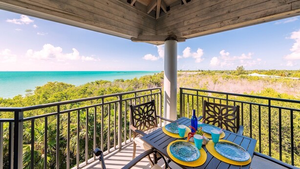 Een balkon met een tafel voor twee personen, met uitzicht op een strand en de oceaan.