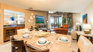 Een eetgedeelte met een tafel voor vier personen, een keuken met een wijnkoeler, en uitzicht op de oceaan door een schuifdeur.