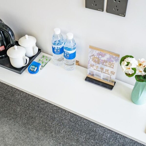A hotel reception desk with a kettle, teapots, bottled water, a small card, and a vase with flowers. - Floral Hotel Cun Zi Li Chengdu (Hangzhou)