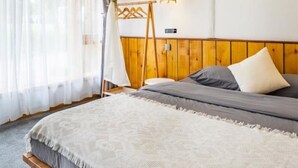 A bedroom with a bed, a wooden headboard, a hanging light fixture, and a window with sheer curtains.
