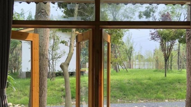 A room with large glass doors leading to an outdoor area with a wooden deck and greenery.