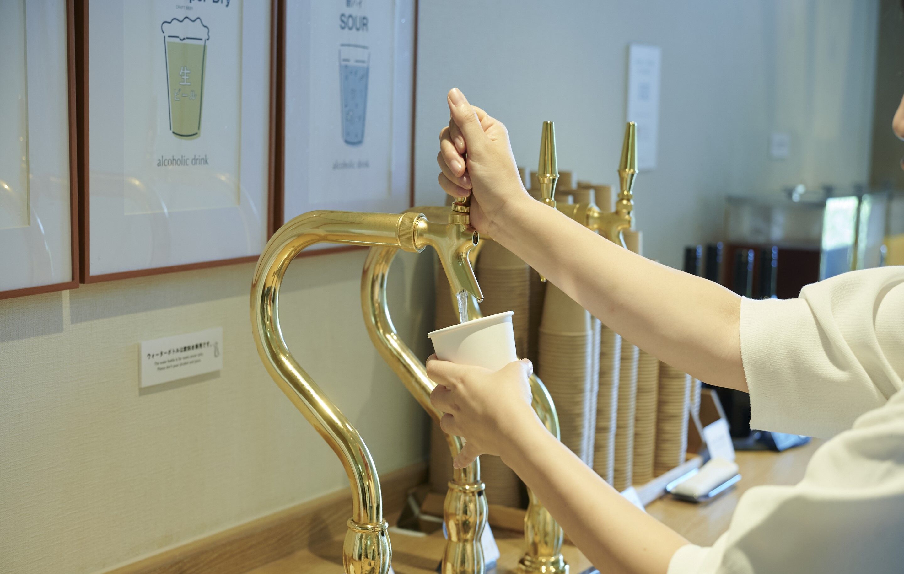 A hand filling a paper cup from a gold-colored faucet.