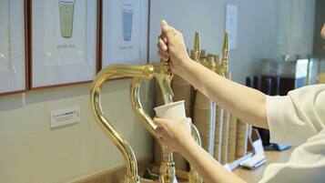 A hand filling a paper cup from a gold-colored faucet.