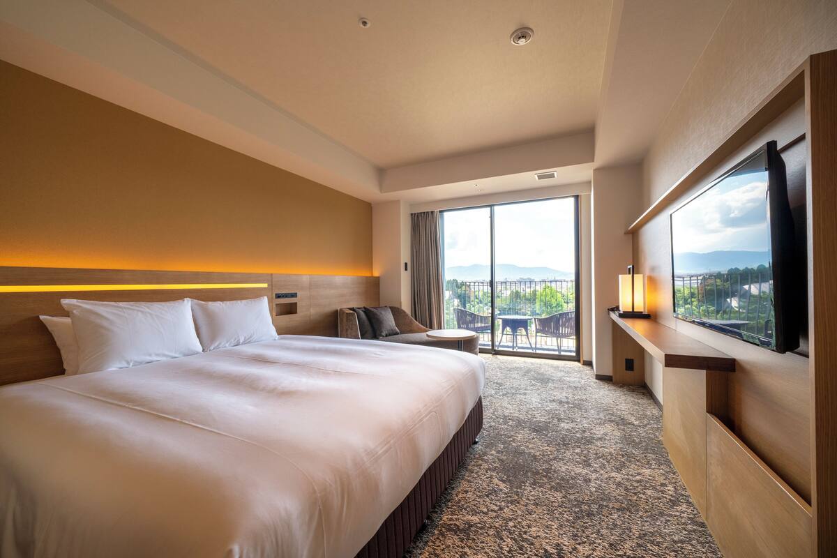 Una habitación de hotel con una cama grande, un área de descanso con vistas y un balcón.
