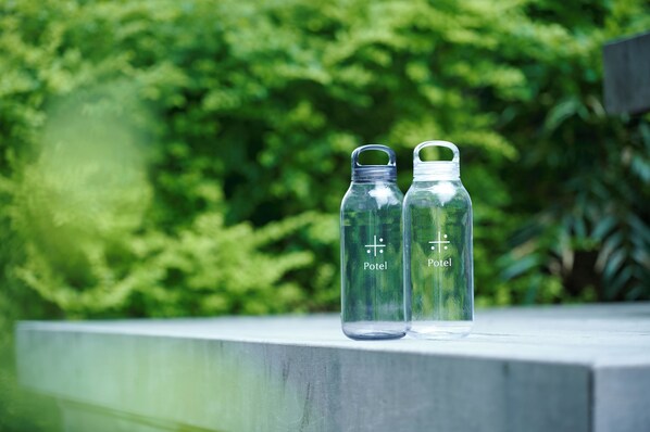 Two clear glass bottles with the word "Potel" on them, placed on a concrete ledge with a blurred green background. - Umekoji Potel KYOTO (Kyoto)