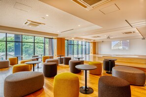A spacious indoor area with multiple seating arrangements, large windows, and a modern ceiling design.