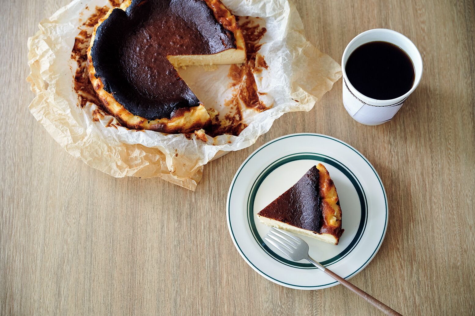 Uma fatia de torta em um prato com um garfo ao lado, uma xícara de café e uma torta com crosta sobre uma mesa de madeira.