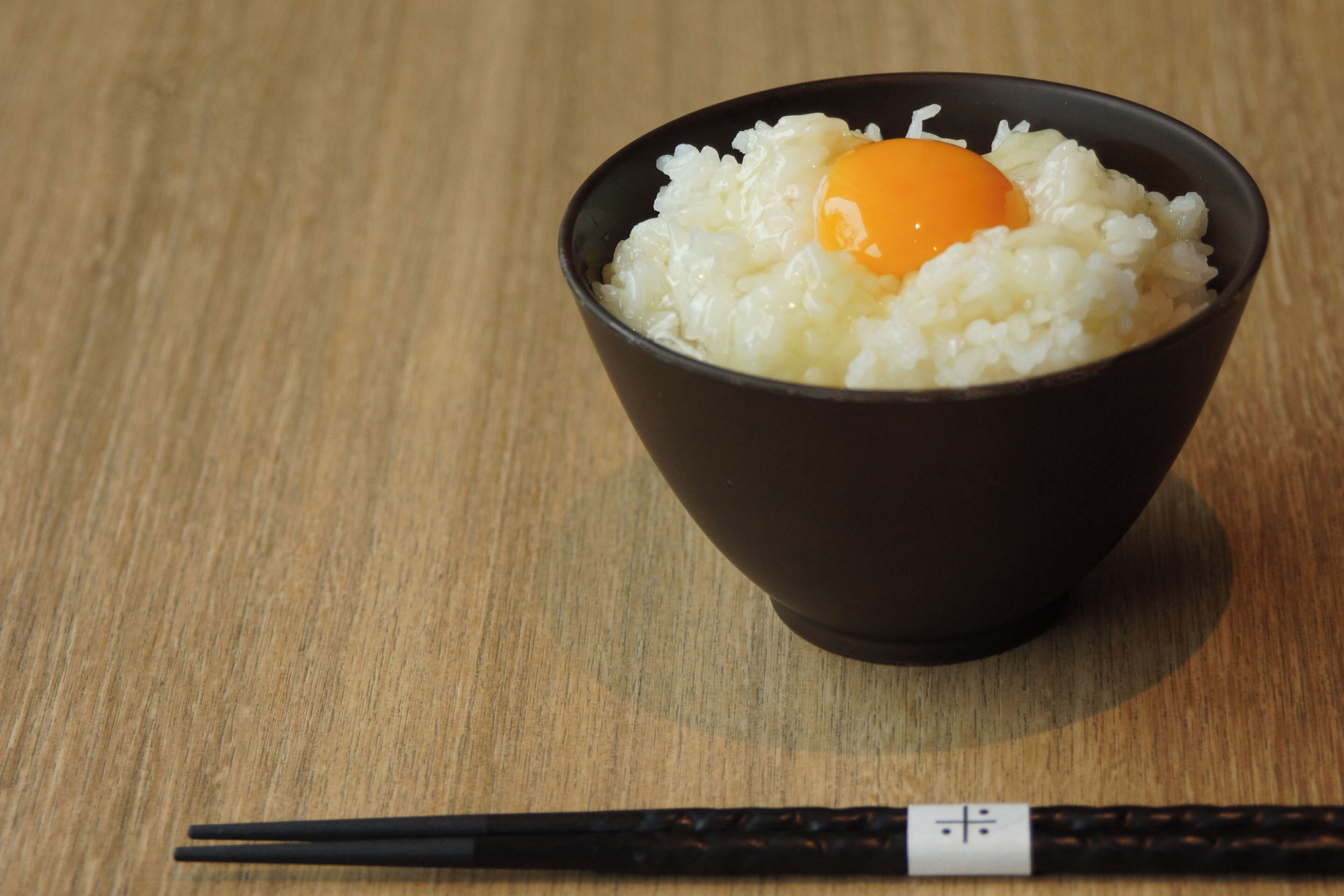 A bowl of rice with an egg on top, placed on a wooden table.