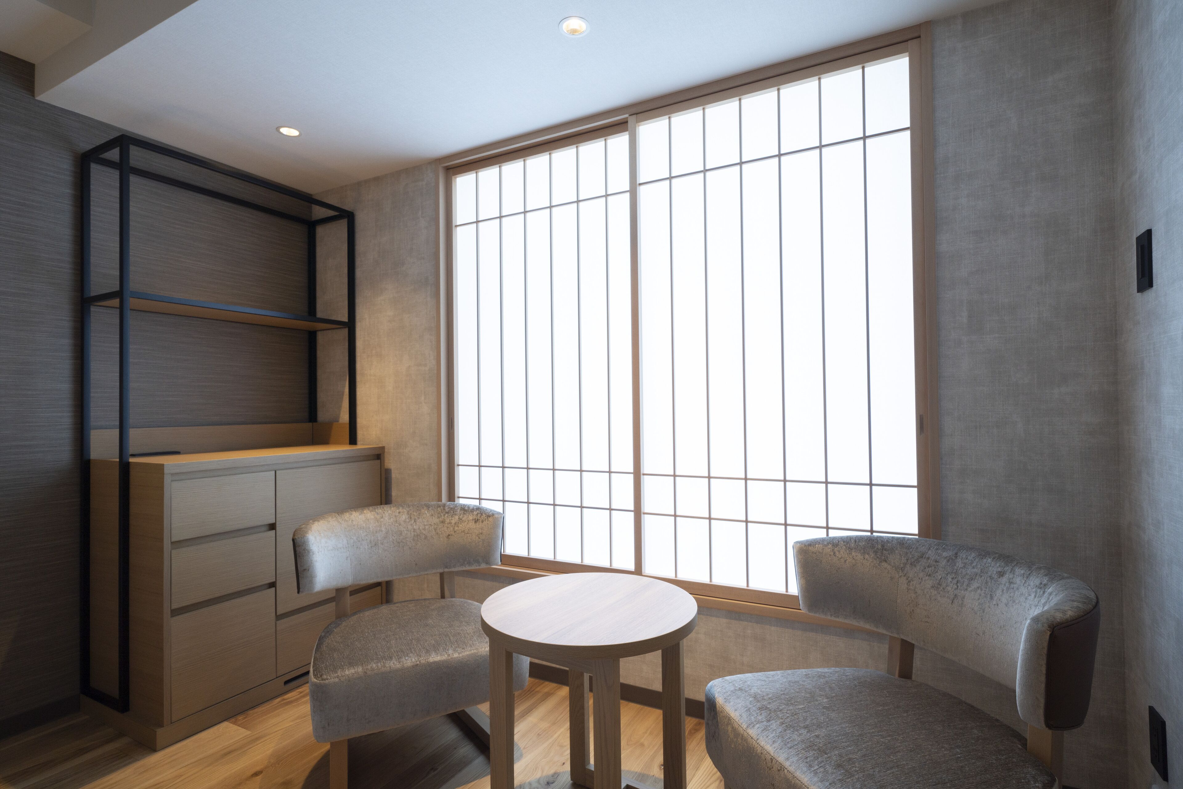 A room with a large window, a wooden cabinet, and two chairs.