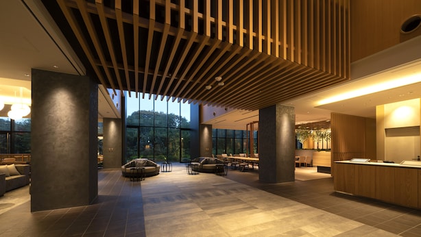 Un vestíbulo espacioso con diseño moderno, que presenta un techo de madera, ventanas amplias y una zona de recepción.
