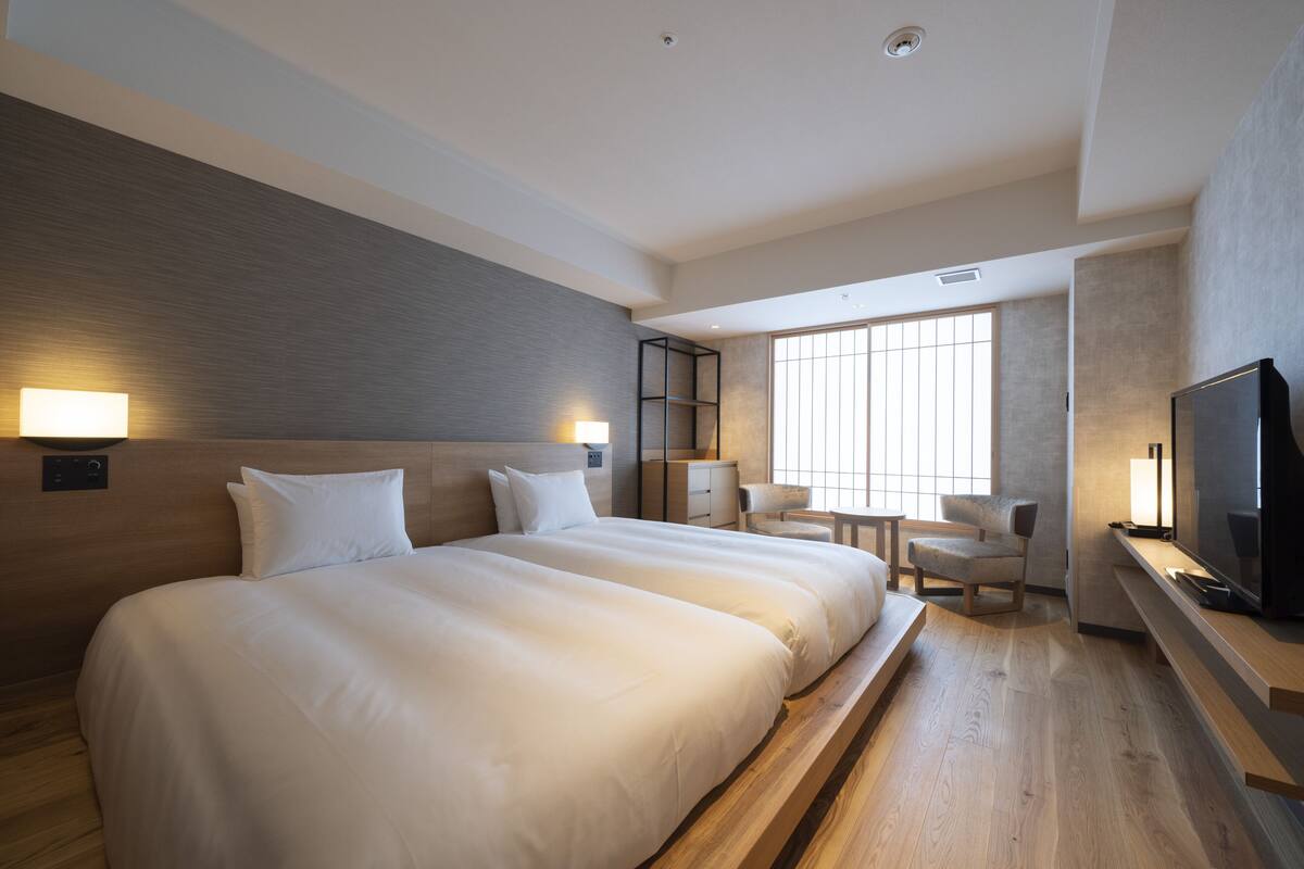 Habitación de hotel con dos camas, televisión, escritorio y una silla.