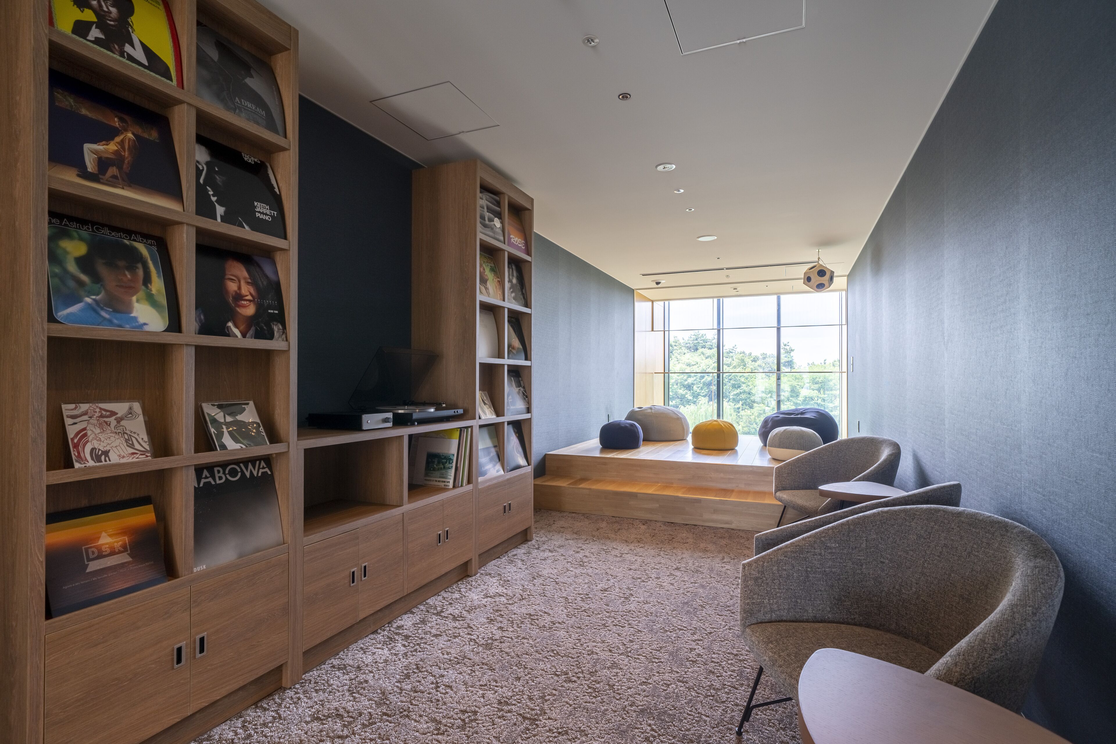 A modern room with a large wooden bookshelf, a comfortable seating area with chairs and a small table, and a large window providing natural light.