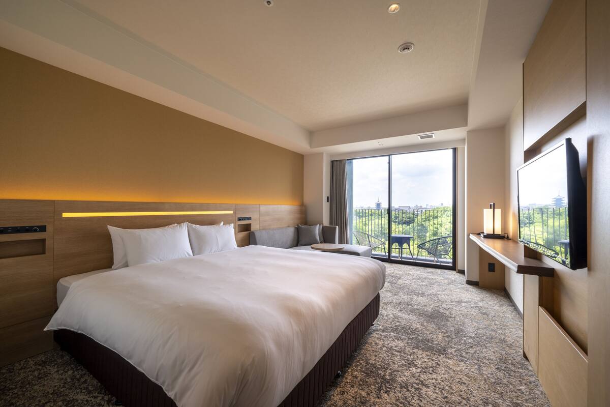 Una habitación de hotel moderna con una cama grande, un televisor de pantalla plana, un balcón con vistas a la ciudad y un amplio ventanal.