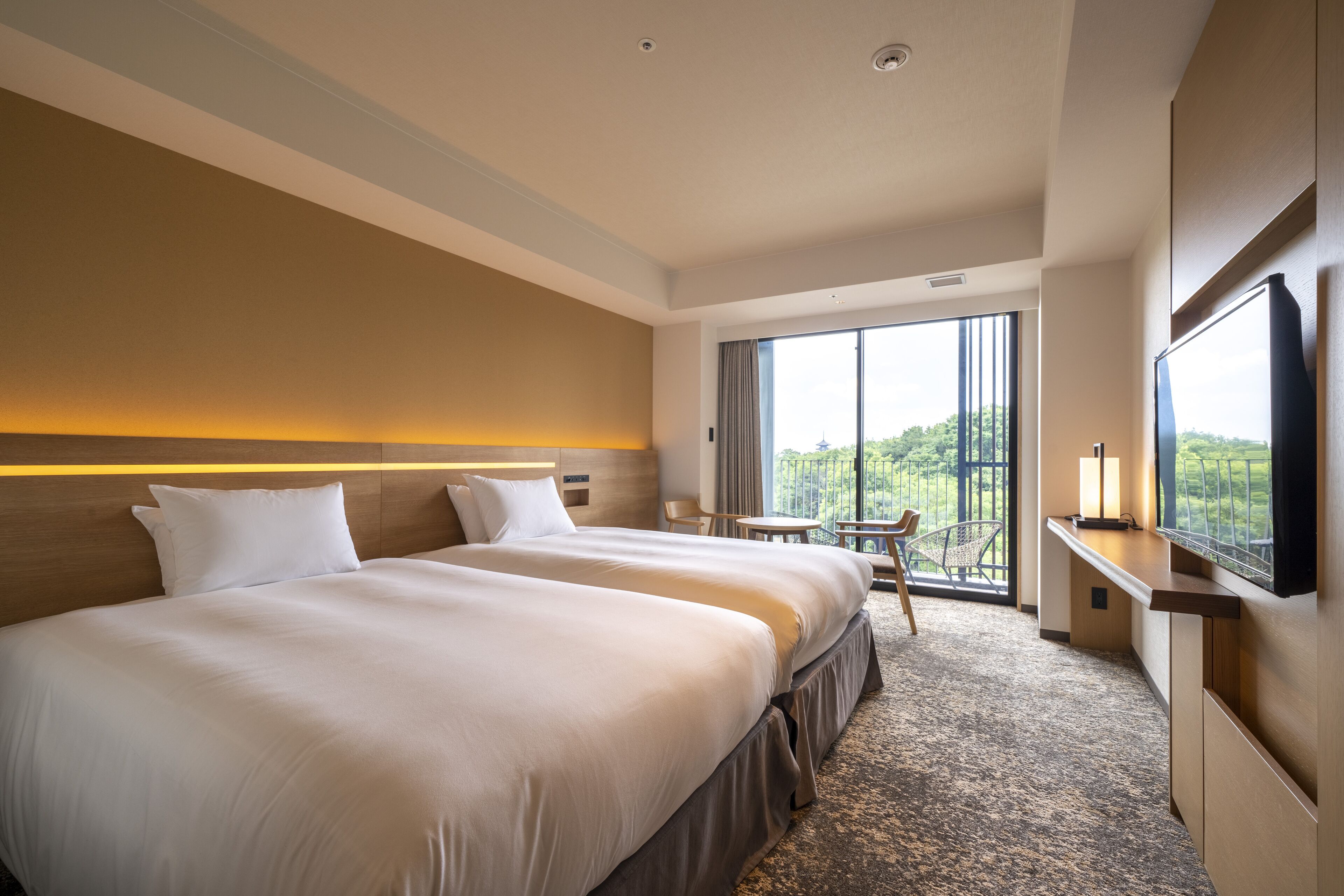 A hotel room with two beds, a desk, a chair, and a large window offering a view.