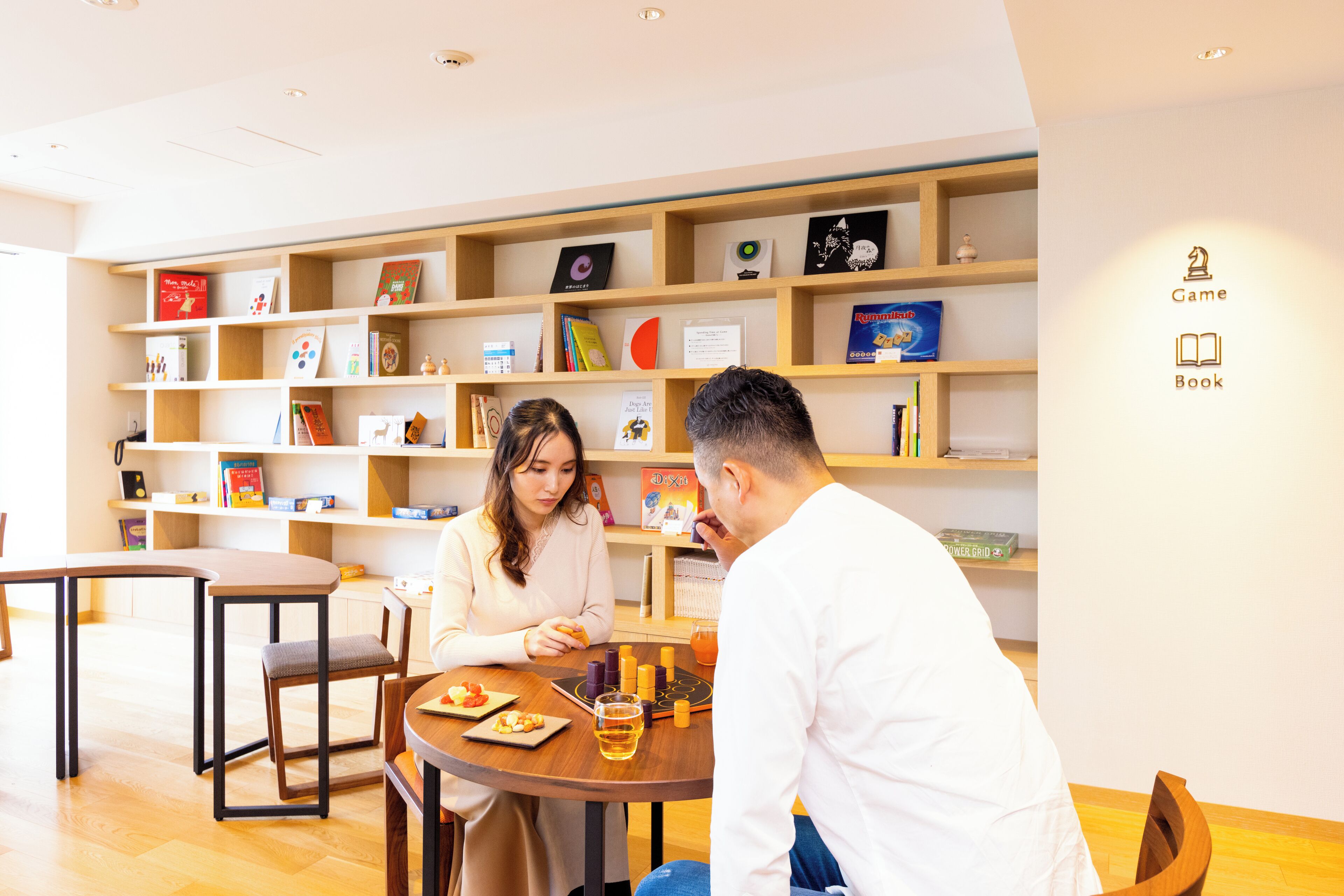 A modern interior with a round wooden table, chairs, and a bookshelf filled with books and decorative items.