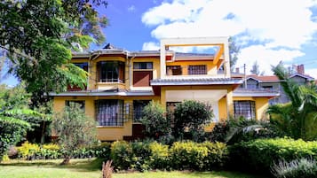 Uma casa de dois andares com varanda, cercada por vegetação exuberante e um gramado bem cuidado.