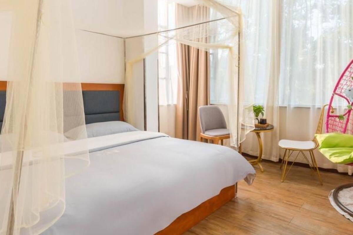 Une chambre d’hôtel avec un lit, une chaise, une petite table et une fenêtre avec des rideaux.
