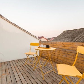 A wooden deck with yellow chairs and a small table, overlooking a cityscape.