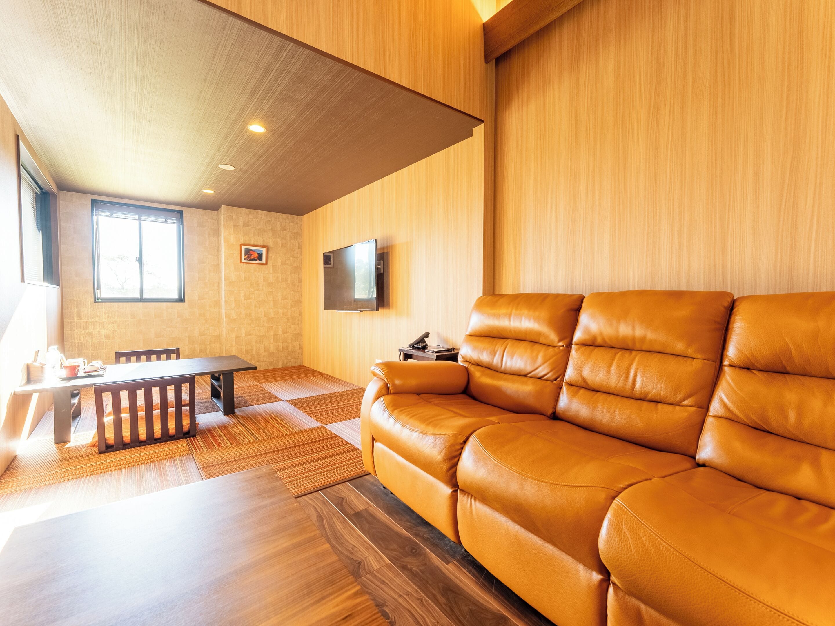 A modern living room with a leather sofa, a dining table, and a TV mounted on the wall.