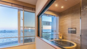 A modern bathroom with a glass-enclosed bathtub, a view of the sea, and a wooden floor. - LiVEMAX RESORT Sakurajima-seafront (Tarumizu)