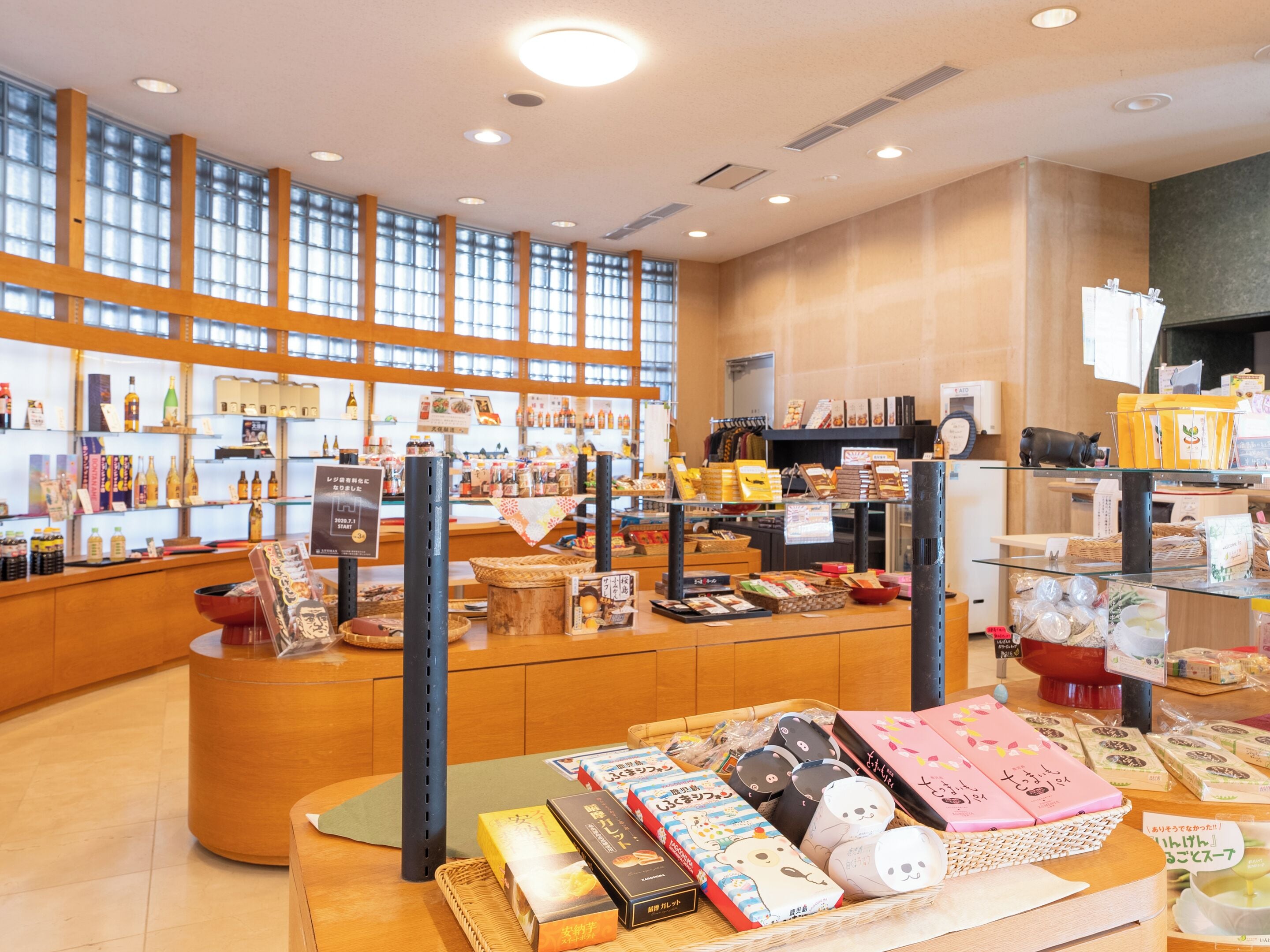 Una tienda amplia con piso de madera y ventanas grandes, estantes llenos de diversos productos y un mostrador con una exhibición de artículos.