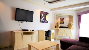 Ein Hotelzimmer mit an der Wand montiertem Fernseher, einem Schreibtisch mit Stuhl, einem kleinen Tisch, einer Couch und einem dekorativen Spiegel.