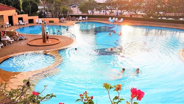 Ein großes Schwimmbecken im Freien mit mehreren Bahnen, umgeben von Liegestühlen und einem kleineren Poolbereich.