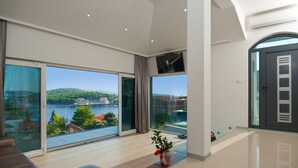 A spacious living room with large windows offering a view of a lake and buildings. - Villa Martinis (Rogoznica)