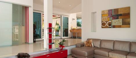 Een moderne woonkamer met een bruine leren bank, een kast in rood en wit en een glazen deur naar een balkon.