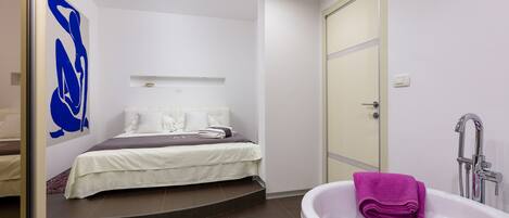Un dormitorio moderno con cama, baño con bañera y un cuadro abstracto de gran tamaño en la pared.