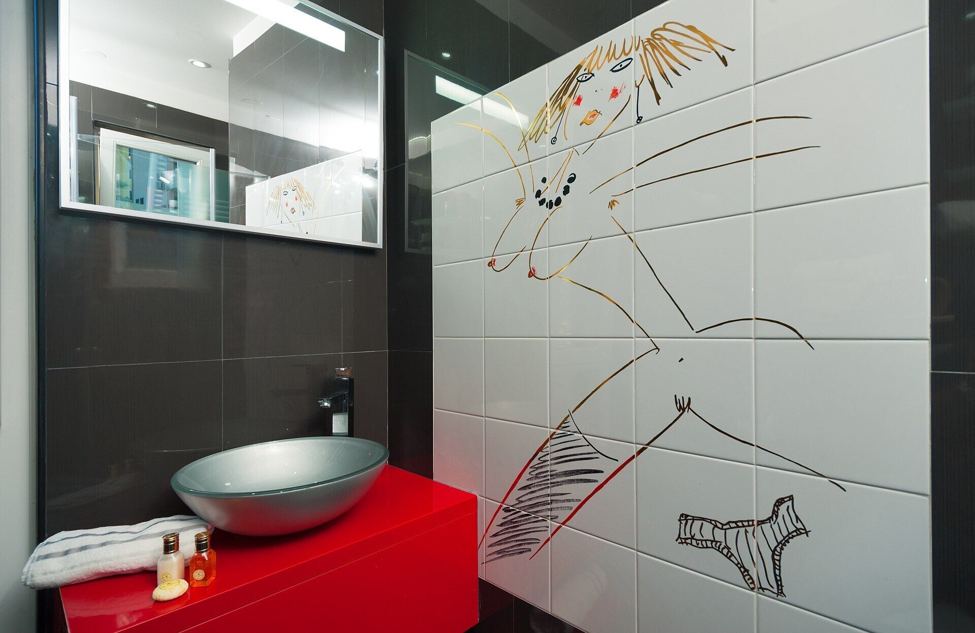 Un baño moderno con un espejo grande, una encimera roja y un lavabo blanco.