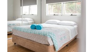 A neatly made bed with a patterned bedspread and two rolled towels, a wooden floor, and a large mirror reflecting the room. - Picturesque on Passage - Whitsundays (Shute Harbour)