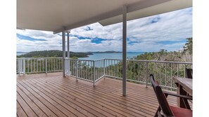 Une terrasse en bois avec une balustrade blanche, donnant sur une étendue d’eau et sur une terre lointaine.