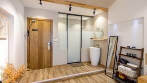 A modern bathroom with a wooden door, a glass shower enclosure, a large mirror, and a wooden shelf with toiletries. - Floral Hotel Yipin Visual Arts Xitang (Jiaxing)
