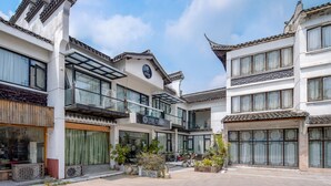 A traditional-style hotel with multiple floors, large windows, and a balcony with outdoor seating. - Floral Hotel Yipin Visual Arts Xitang (Jiaxing)