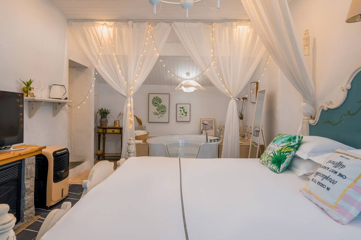 Un dormitorio con cama, televisor, chimenea y baño visible a través de una entrada cubierta con cortinas.