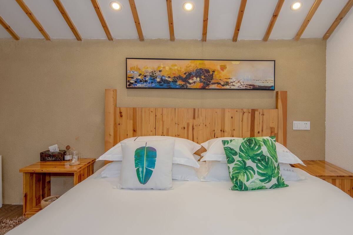 Habitación de hotel con cabecera de madera, un cuadro sobre la cama y una mesita de noche con una caja de pañuelos y un objeto decorativo.