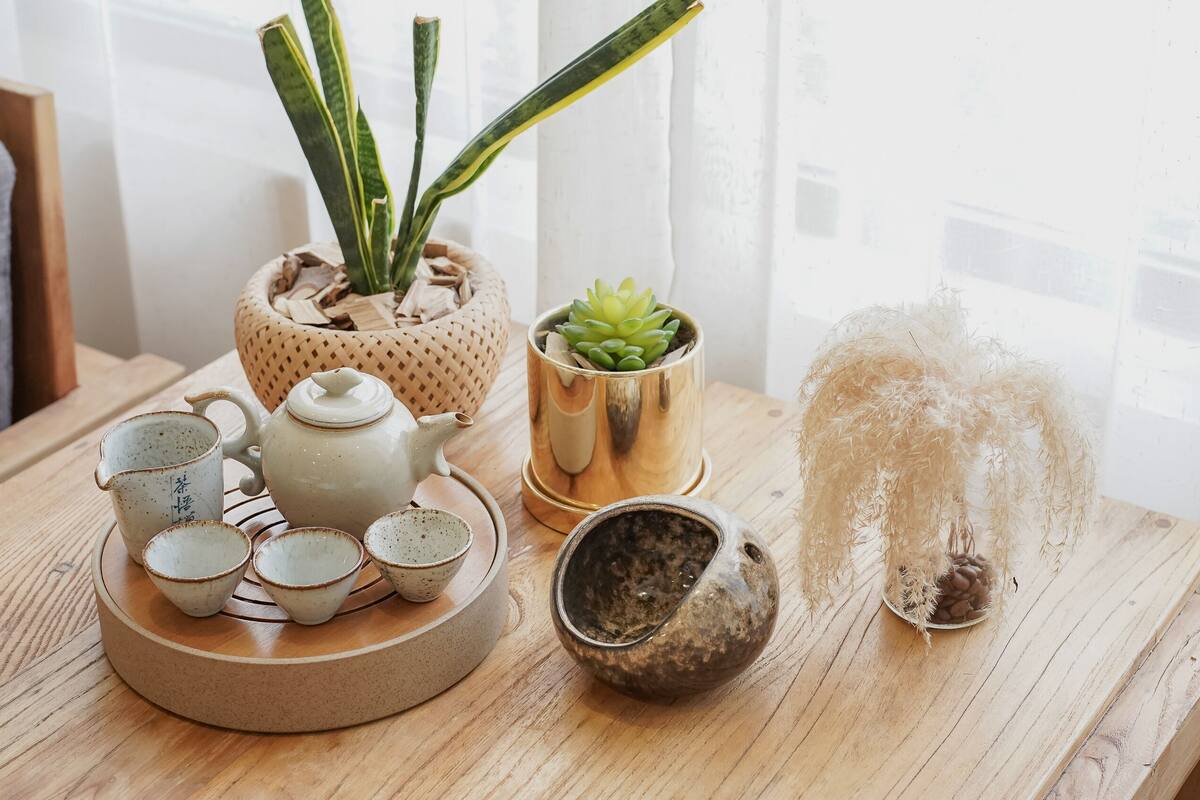 Una mesa de madera con una tetera, tazas, una planta suculenta y un adorno.