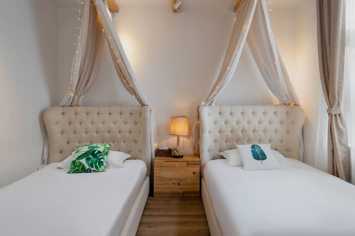 Una habitación con dos camas, cada una con dosel y mesita de noche con lámpara.