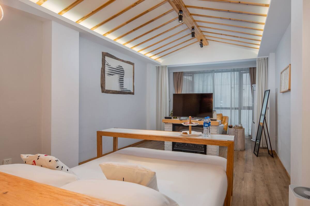 Una habitación de hotel con una cama, un escritorio con computadora, un televisor y un ventanal grande.
