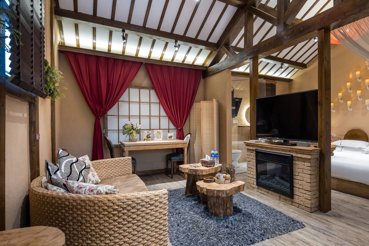 Una habitación acogedora con cama, televisión, chimenea y zona de estar con una silla de mimbre y una mesita.
