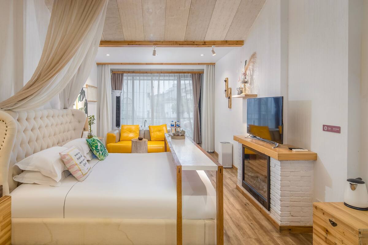 Un dormitorio con cama, televisor, chimenea y ventana con cortinas.
