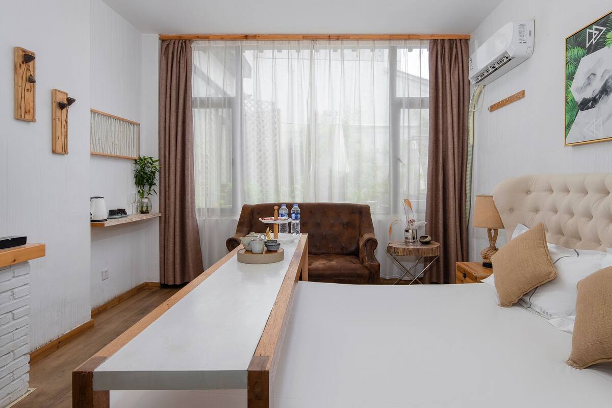 Una habitación de hotel con cama, sofá, televisión, mesa de centro y ventana con cortinas.