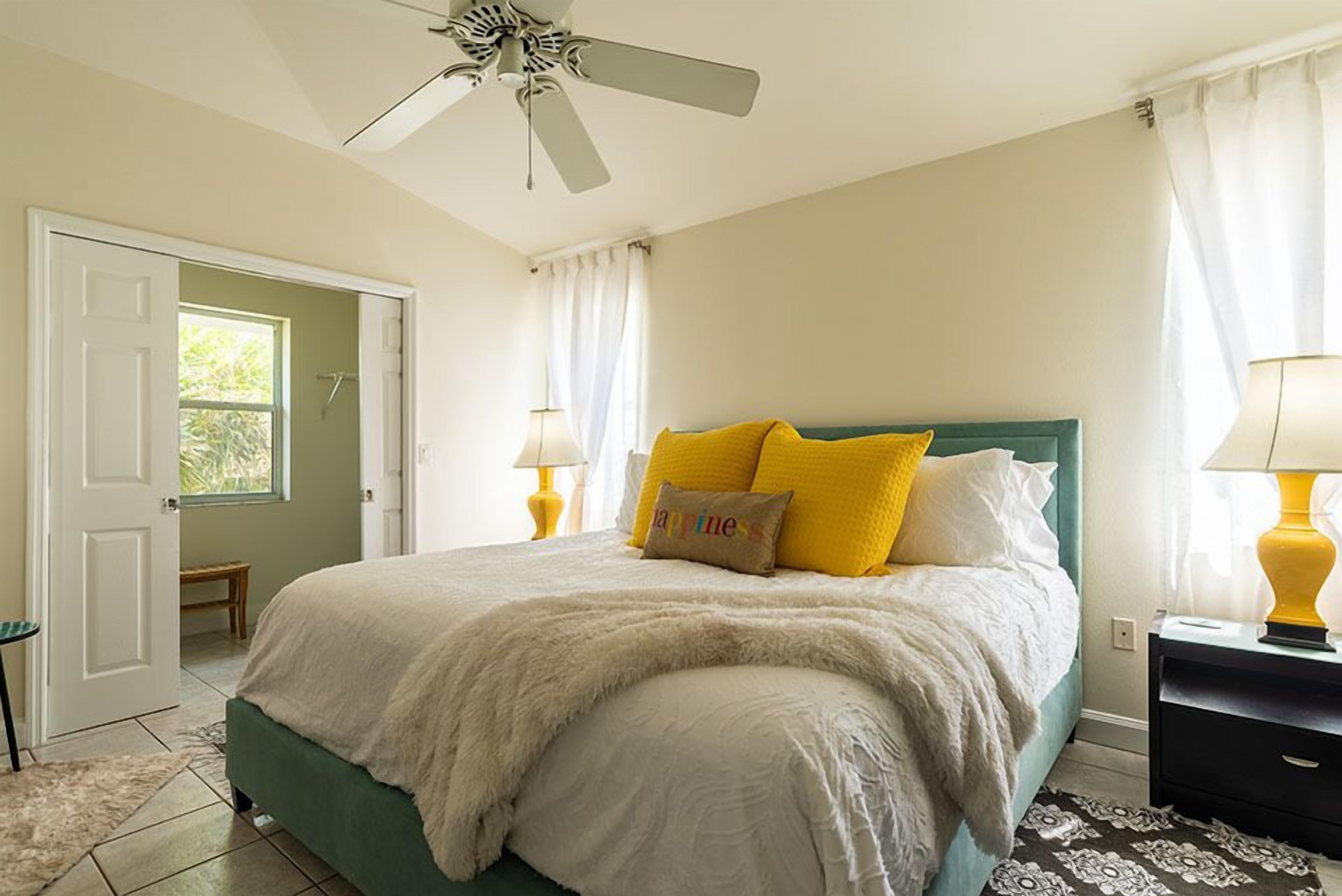 A bedroom with a bed, a ceiling fan, a nightstand, and a door leading to a bathroom.