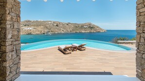 Ein Poolbereich mit Liegestühlen und Blick auf das Meer sowie eine felsige Hügelkuppe.