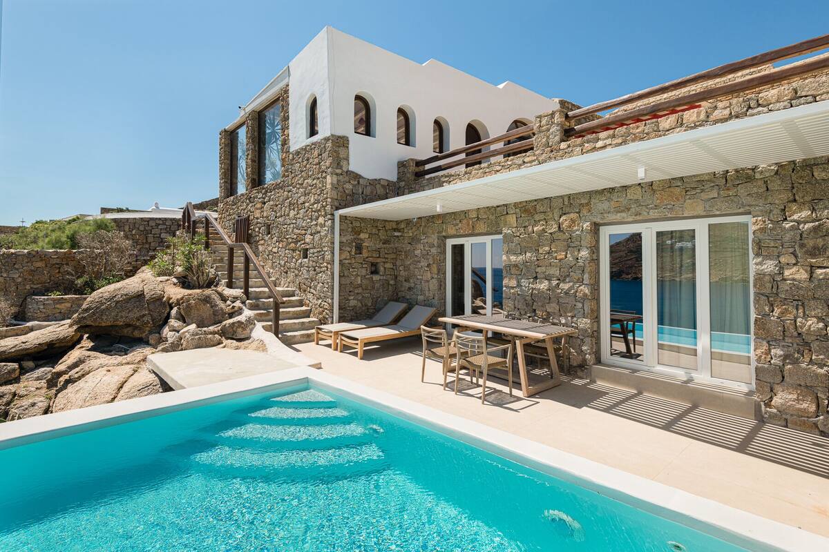 Uma área na piscina com um edifício de pedra, uma piscina e vista para o mar.
