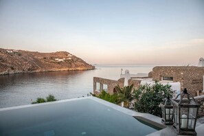 A coastal hotel with an infinity pool overlooking the sea, stone buildings, and a clear view of the coastline.